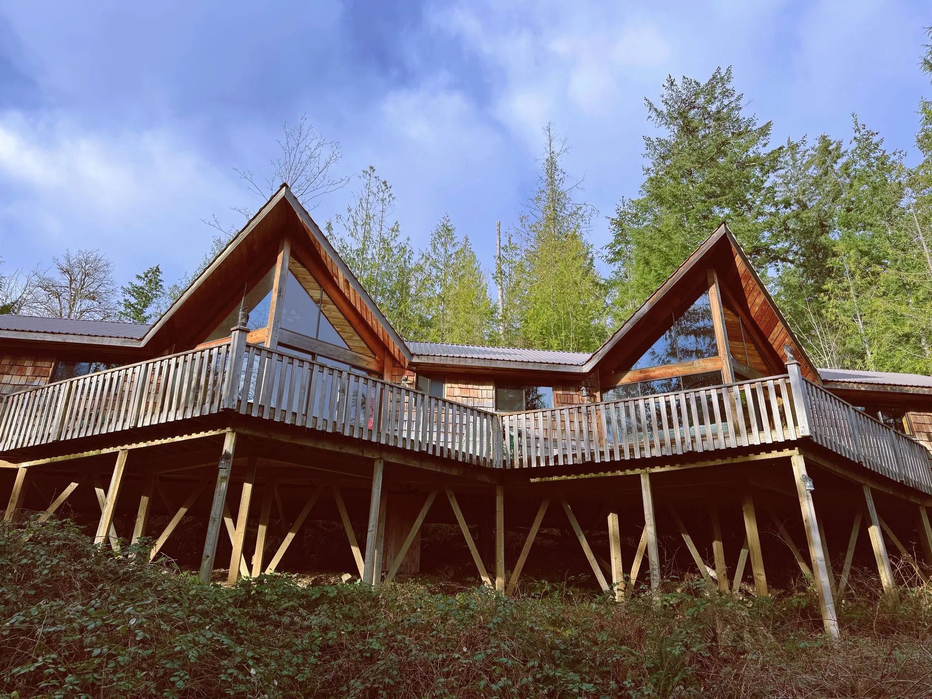 Houten hutten op palen, in de vorm van een A-frame, tussen de bomen onder een blauwe hemel.