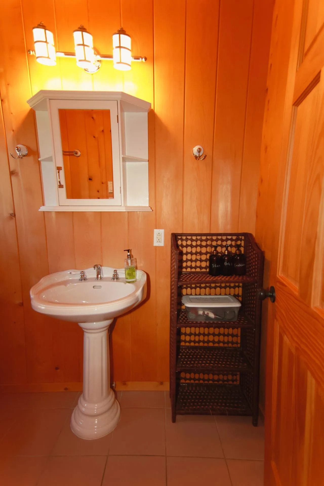 Kleine badkamer met oranje houten lambrisering, wastafel op een voetstuk, spiegel en wandlampen.