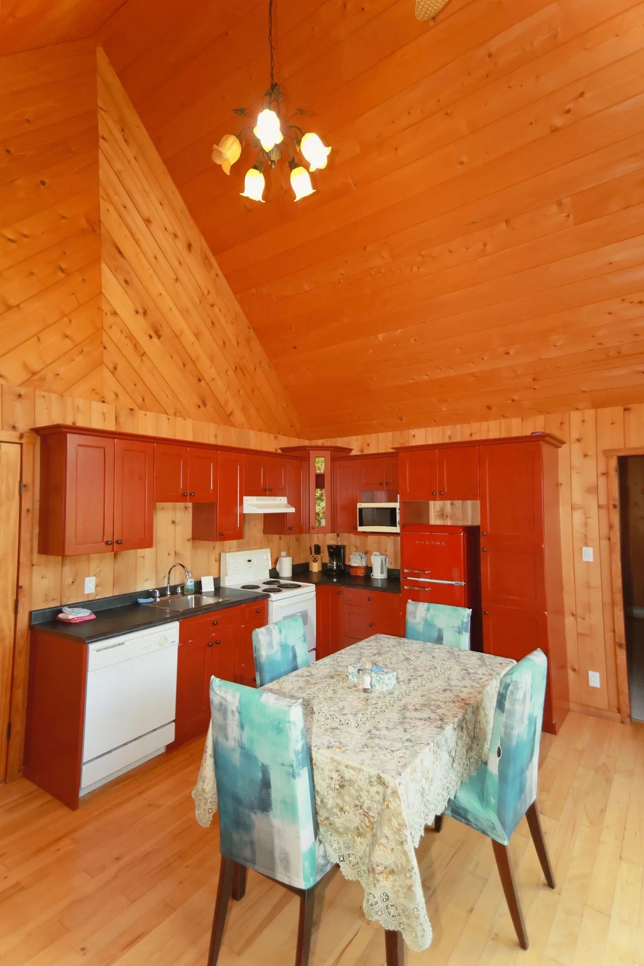Gezellige keuken-eetkamer met houten lambrisering, rode kasten, een eettafel en hanglampen.