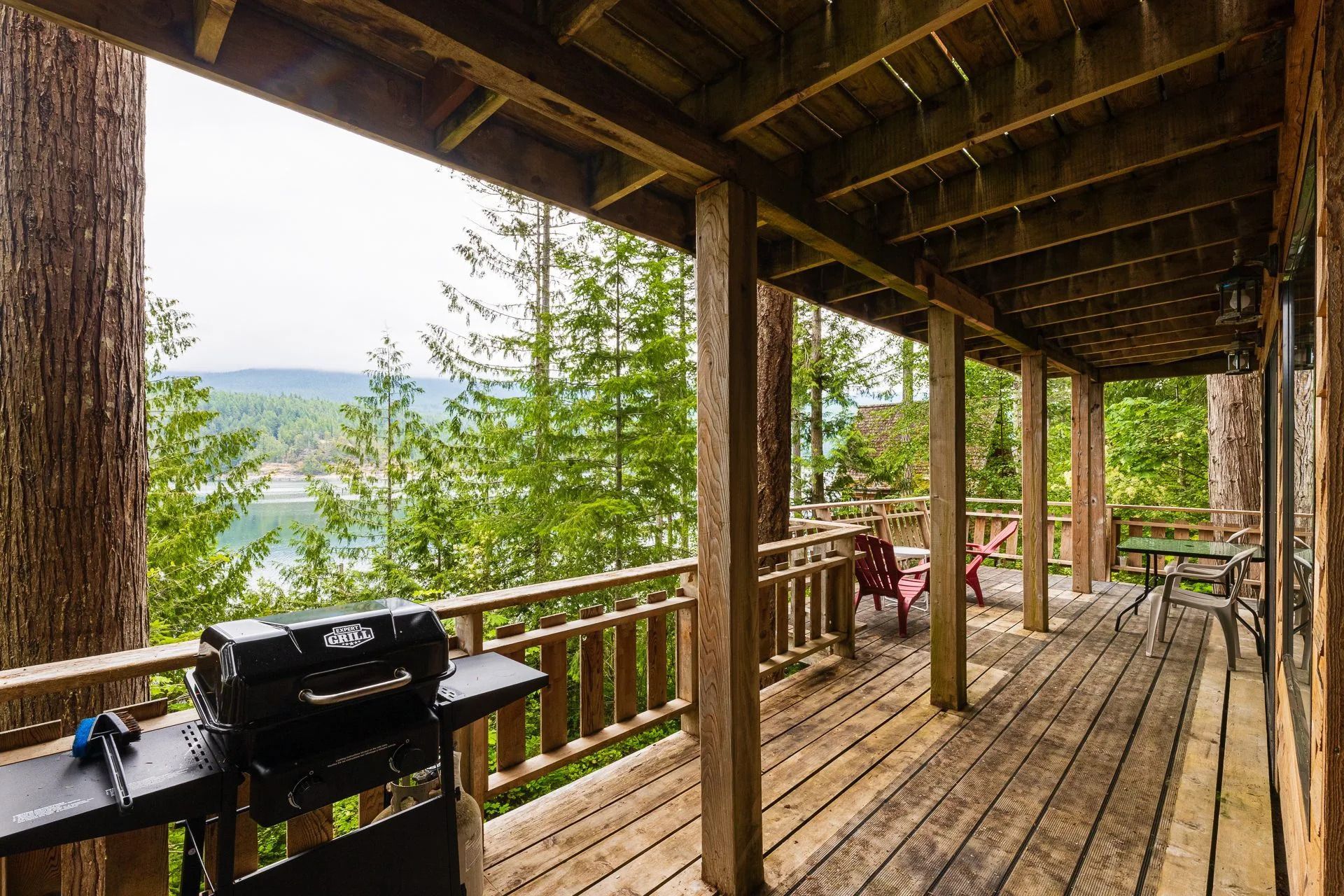 Houten veranda bij de blokhut met barbecue, picknicktafel en uitzicht op het beboste meer.