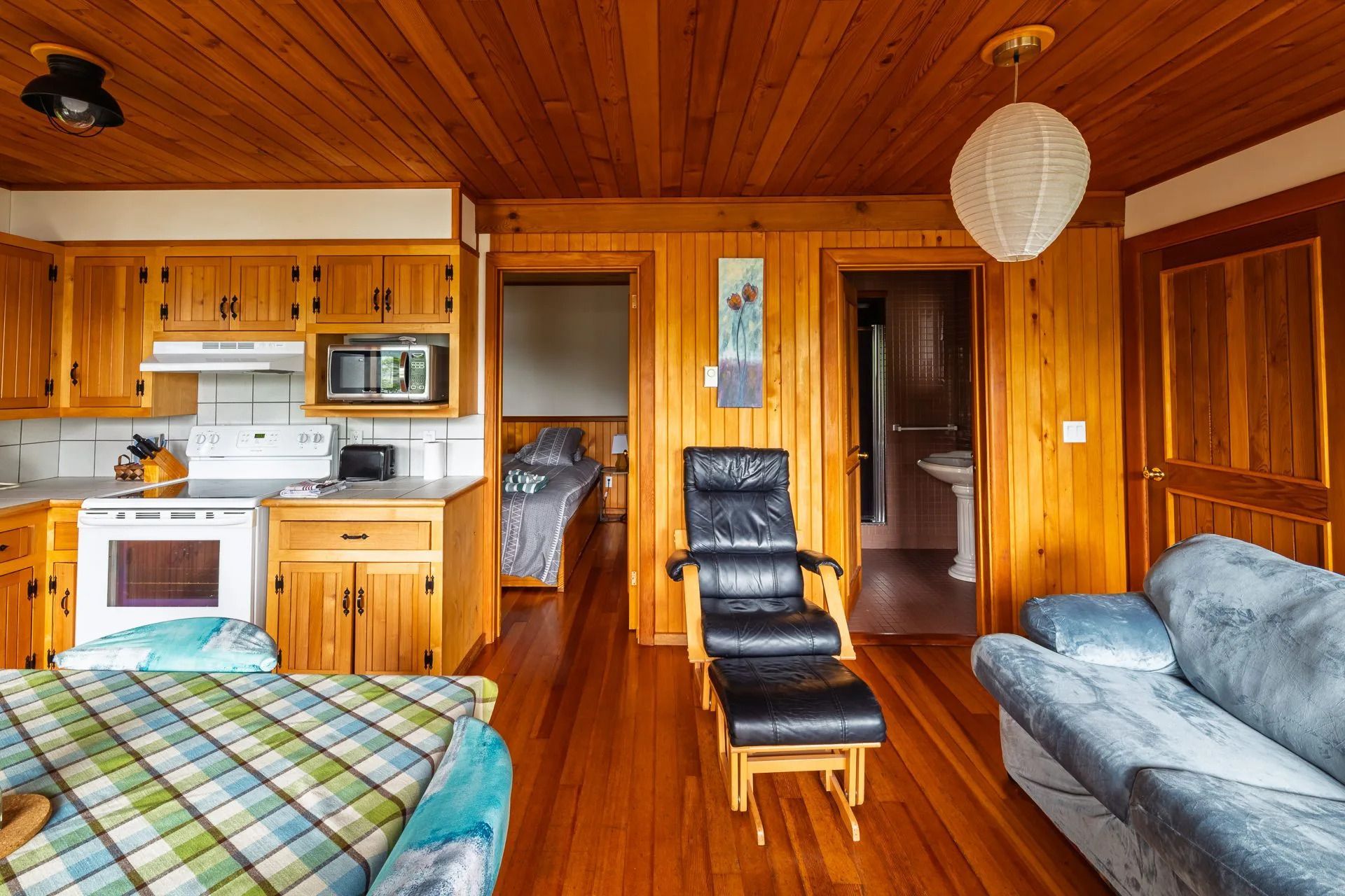 Houten lambrisering in de blokhut, met keuken, bed, relaxfauteuil, bank en een warm houten plafond.