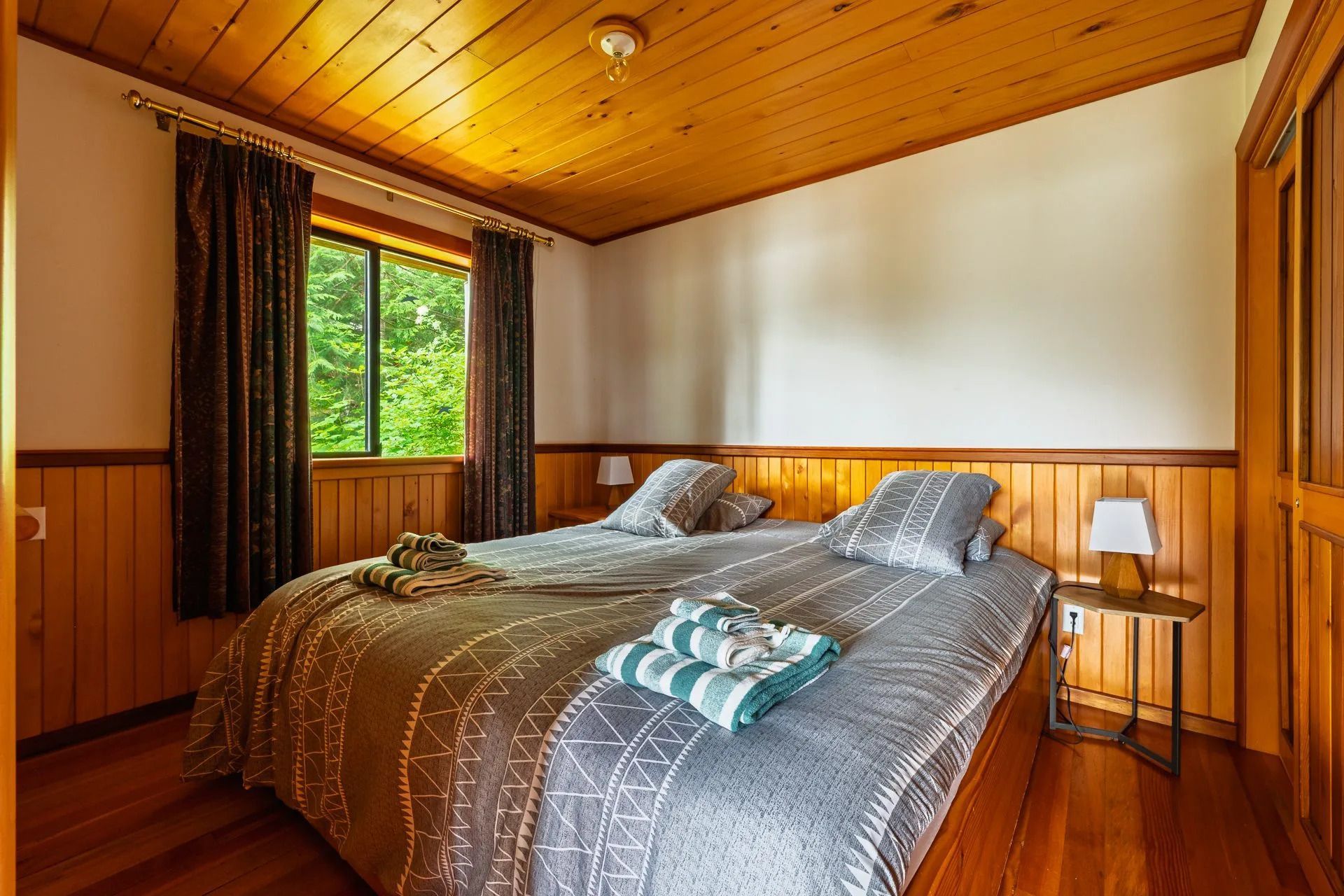 Gezellige slaapkamer met houten lambrisering, een kingsize bed en een groot raam met uitzicht op het groen.