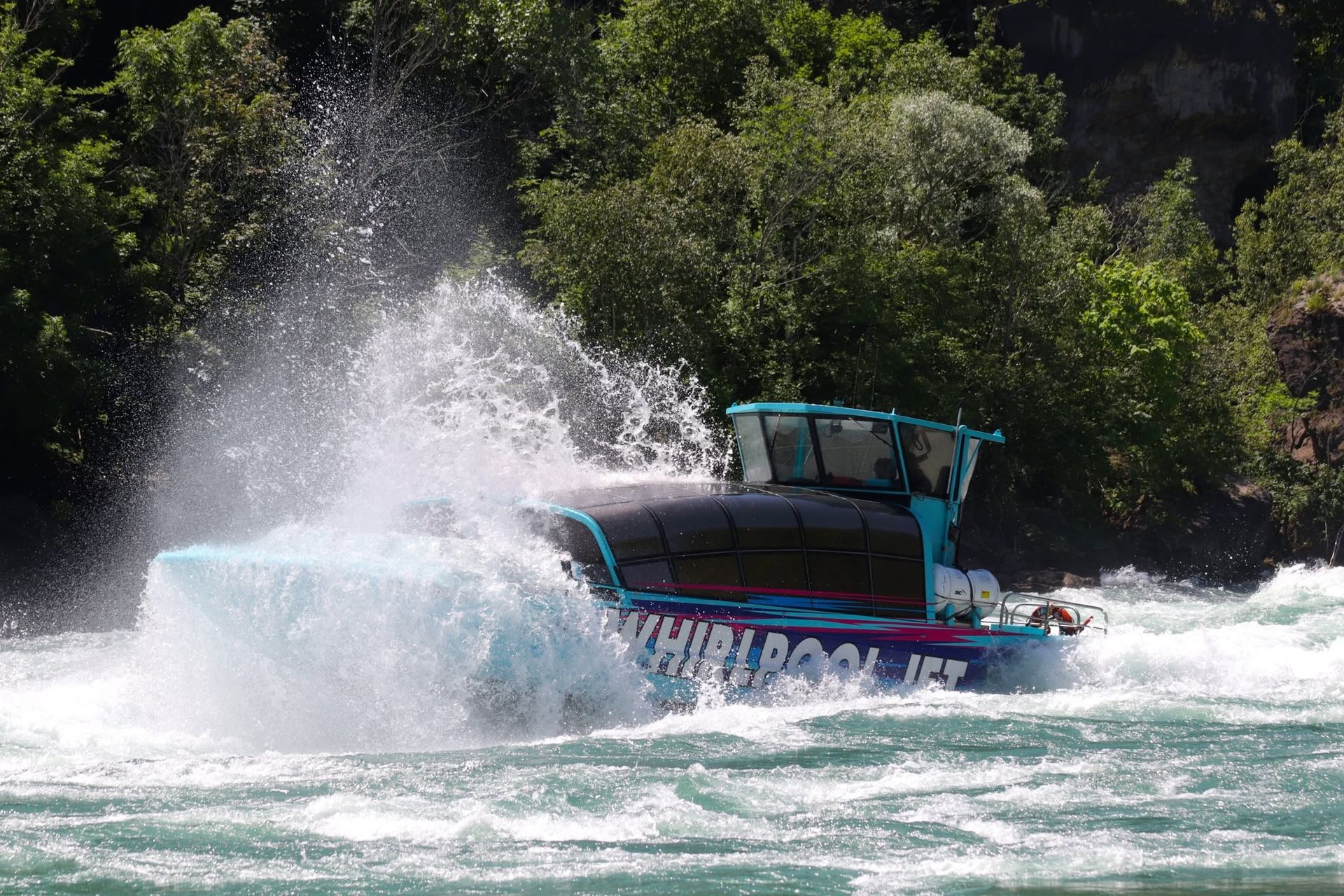 Een speedboot ploetert door het woelige water nabij een beboste kustlijn.
