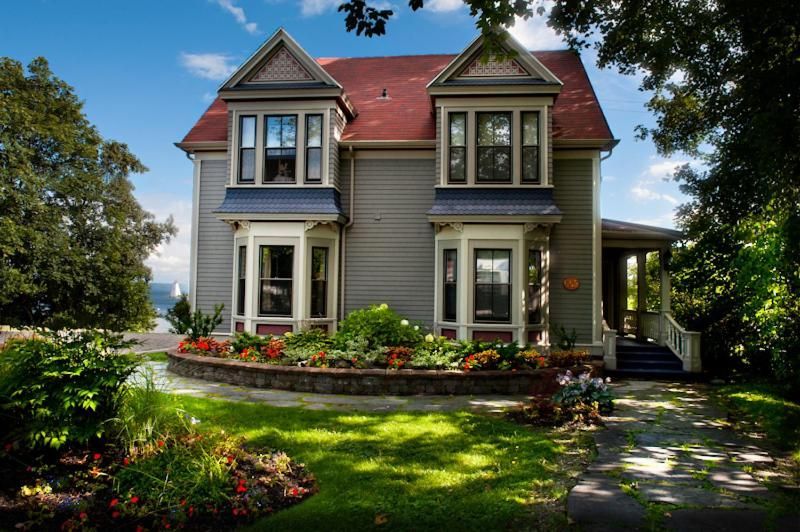 Huis in Victoriaanse stijl met een rood dak, witte kozijnen en een bloementuin in de voortuin.