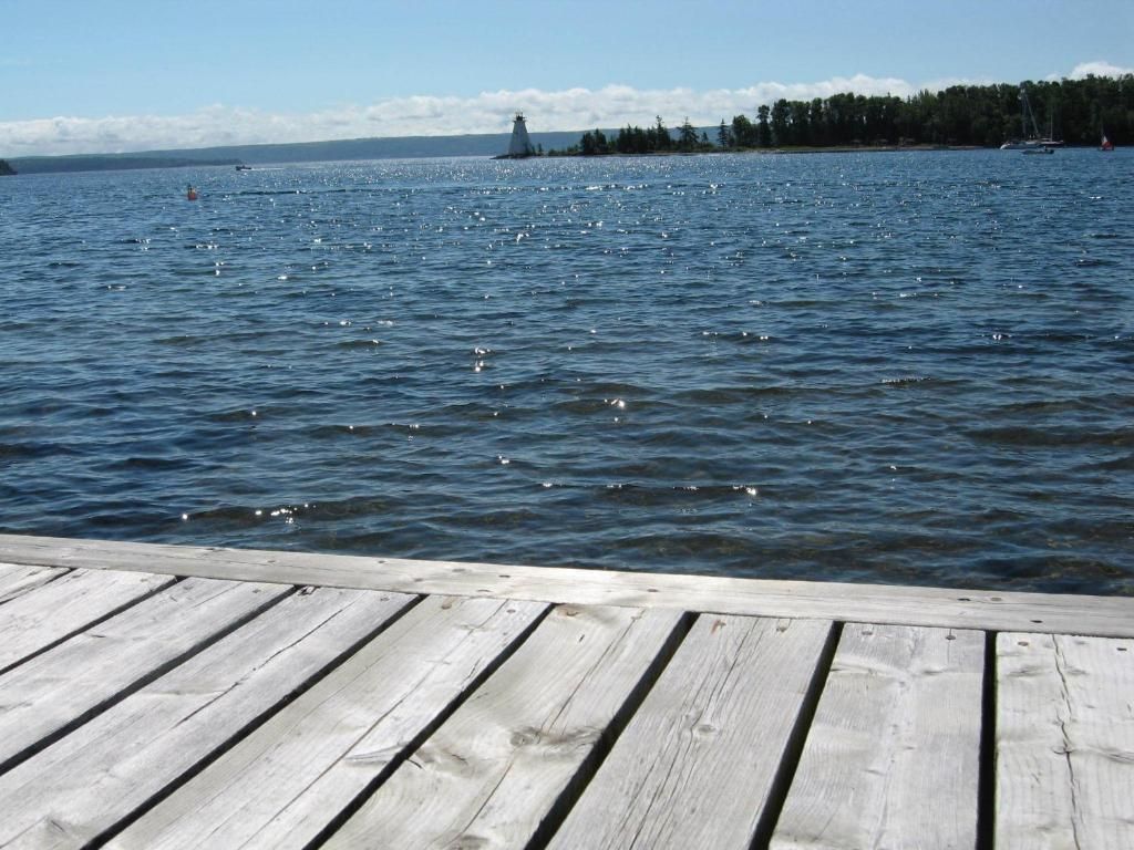 Houten steiger met uitzicht op een kalm blauw meer met de oever in de verte en een heldere hemel.