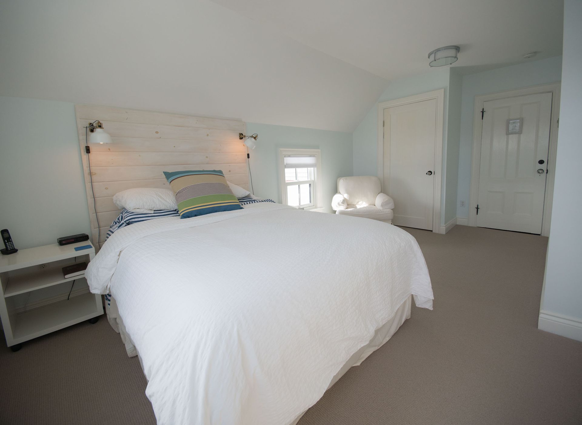 Lichte slaapkamer met een groot wit bed, lichtblauwe muren en een zithoek bij het raam.