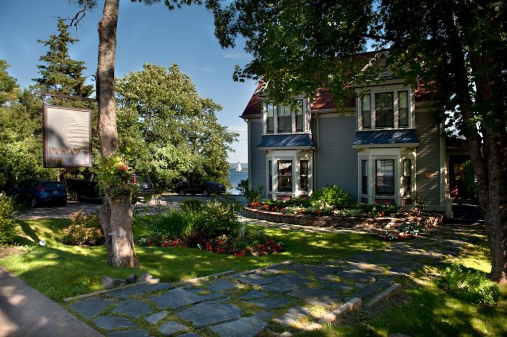 Zonnige tuin met een stenen pad dat naar een blauw huis leidt, omgeven door bomen en bloemen.
