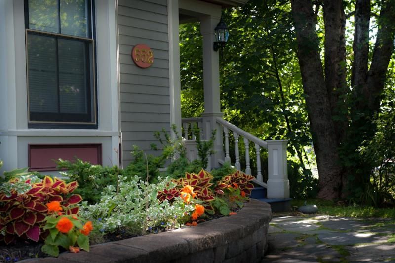 Veranda van het huis met witte balustrade, stenen plantenbak met oranje bloemen en een schaduwrijk tuinpad.