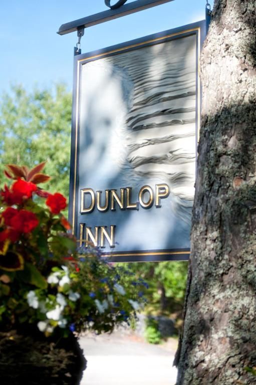 Het uithangbord van Dunlop Inn hangt aan een boom, met rode bloemen op de voorgrond.