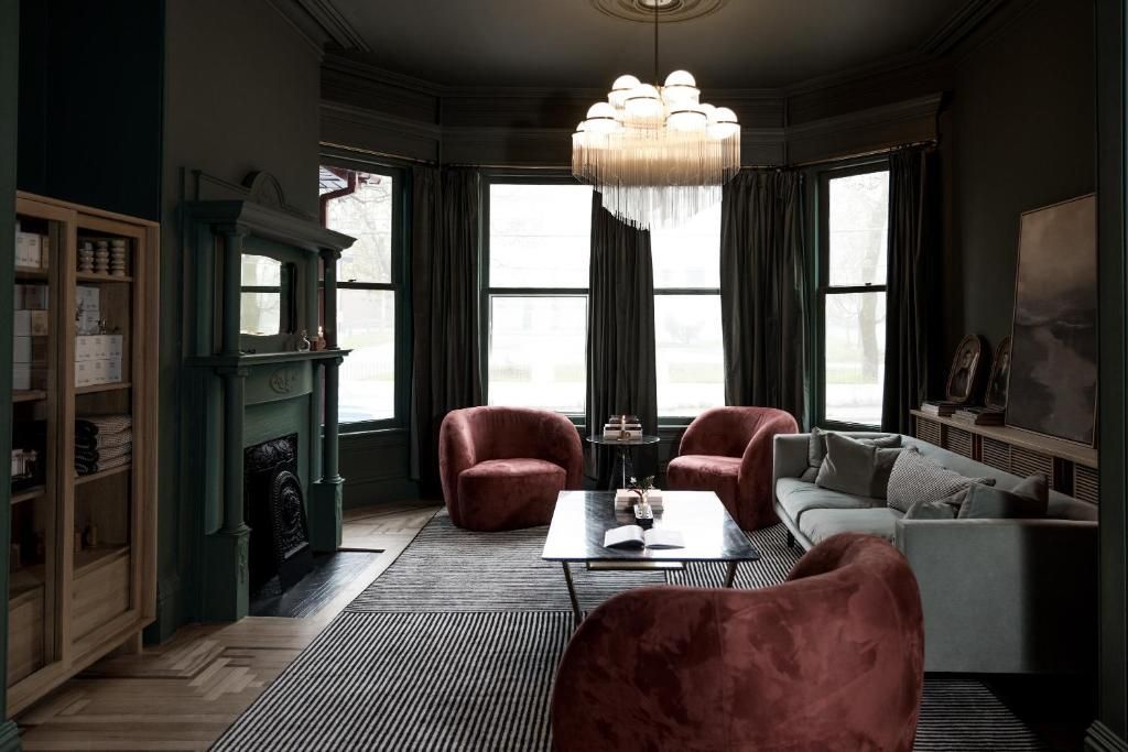 Schemerige woonkamer met rode stoelen, grijze bank, kroonluchter en grote erkers.