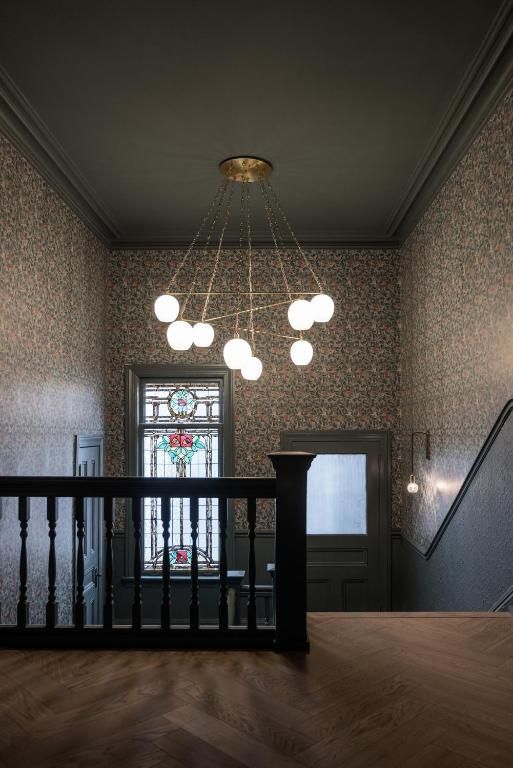 Moderne trappenhal met een zwarte leuning, hangende bolvormige lampen en een glas-in-loodraam boven een houten vloer.