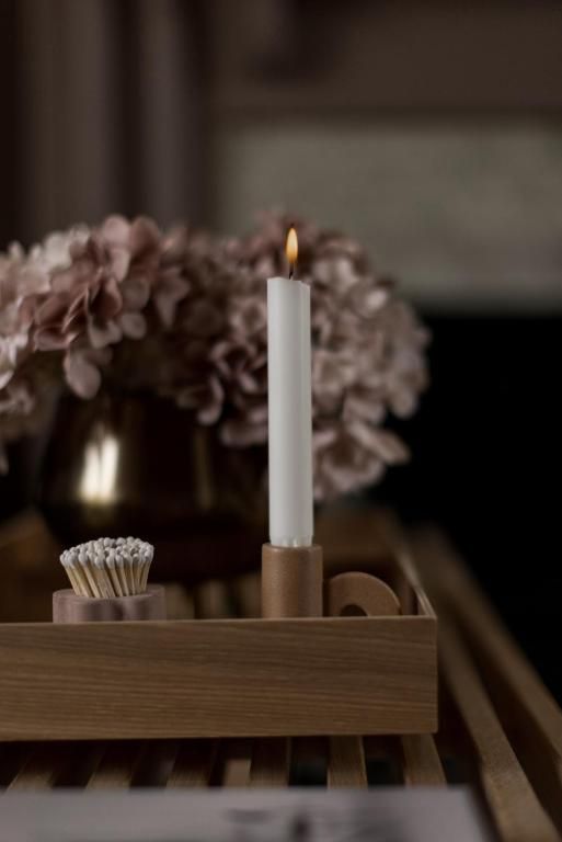 Een brandende witte kaars in een houten houder met een klein boeketje bloemen op de achtergrond.