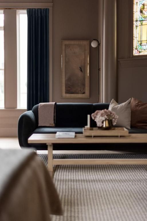 Moderne woonkamer met een zwarte bank, salontafel en een hoog raam met donkere gordijnen.