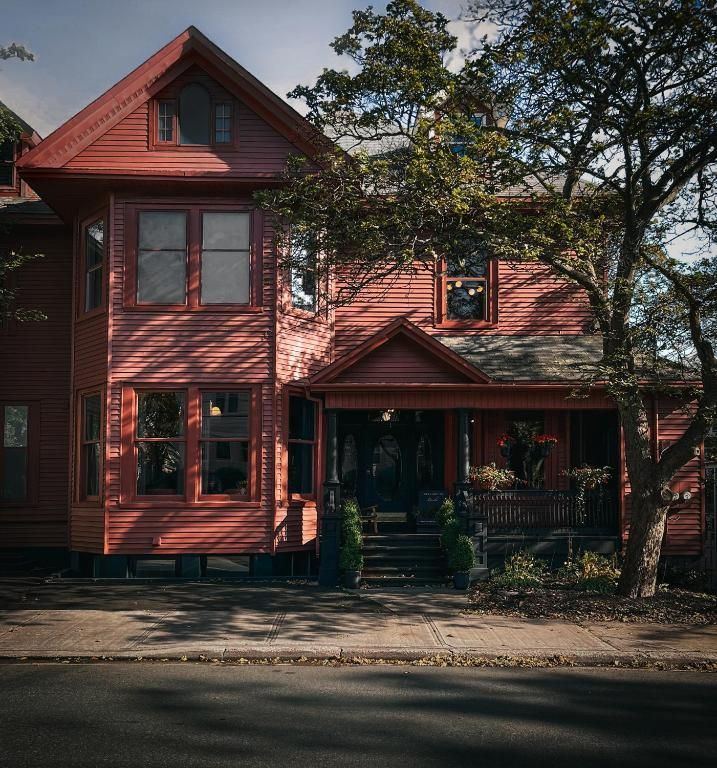 Rood houten Victoriaans huis met veranda en grote bomen langs de straat.