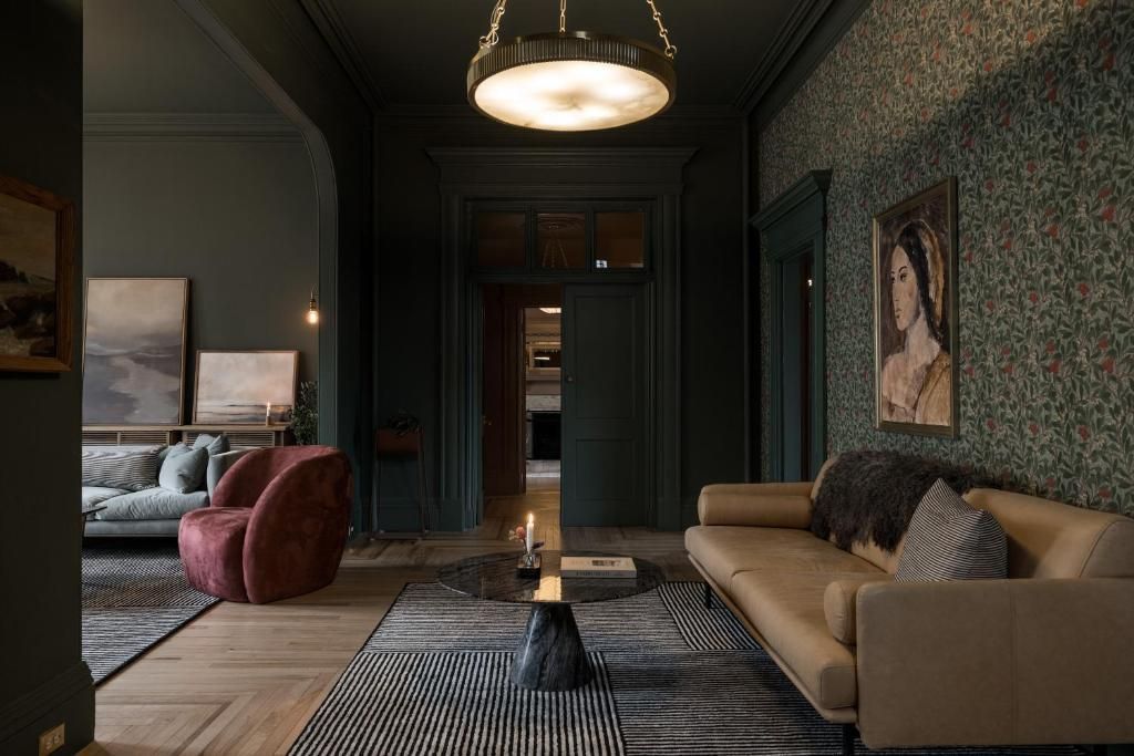 Gezellige woonkamer met een beige bank, rode fauteuil, vloerkleed met patroon en hanglamp tegen schemerige, groene muren.