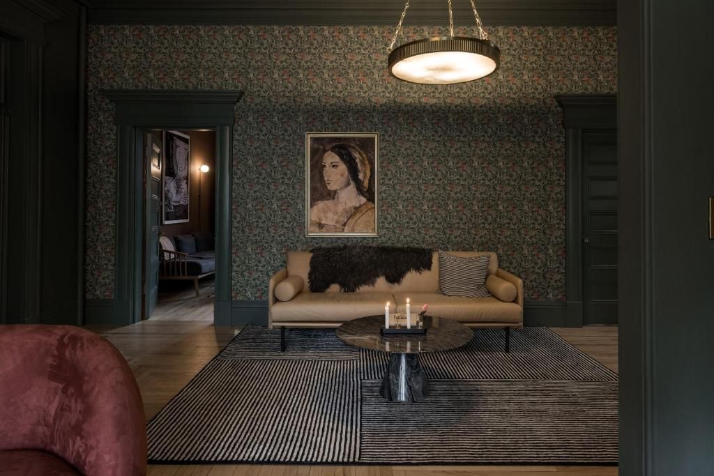 Donkergroene woonkamer met behang met patroon, bank, vloerkleed, salontafel en kroonluchter.