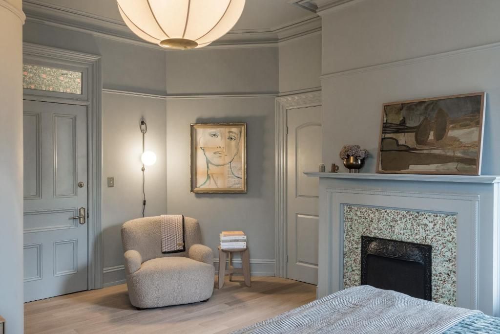 Gezellige slaaphoek met grijze muren, een open haard, een fauteuil en een bed onder een grote plafondlamp.