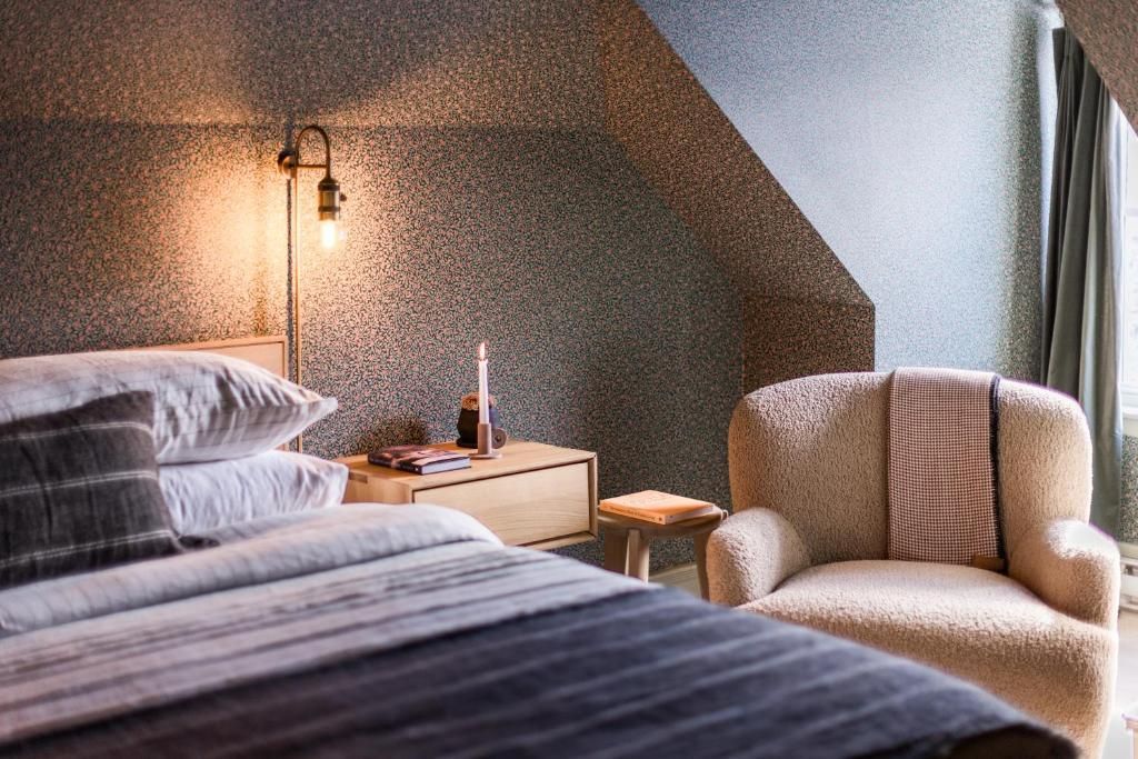 Gezellige slaapkamer met gestreept beddengoed, nachtlampje, houten nachtkastje en beige fauteuil bij het raam.