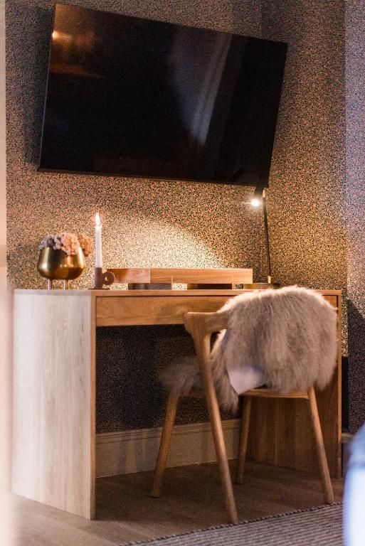 Gezellige bureauhoek met aan de muur gemonteerde tv, houten bureau, stoel met bontplaid en sfeervolle accentverlichting.