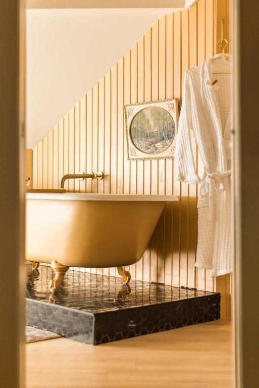 Gouden vrijstaand bad op pootjes in een gestreepte badkamer met een badjas aan de muur.