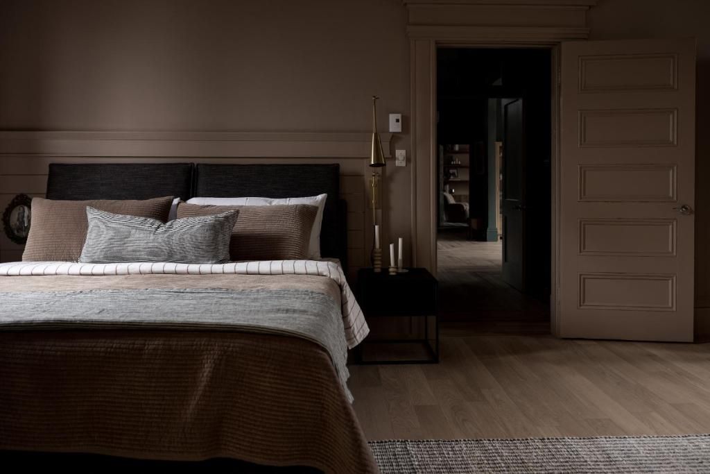 Schemerige slaapkamer met een groot bed, een donkerhouten hoofdbord, een open deur en zachte bruine tinten.
