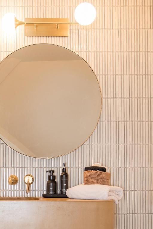 Minimalistische badkamerkast met grote ronde spiegel, wandlamp en netjes opgestapelde handdoeken en toiletartikelen.