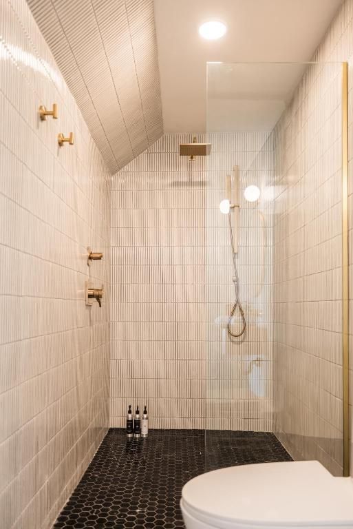 Smalle betegelde douche met zwarte vloer, messing kranen en een glazen scheidingswand in een lichte badkamer.