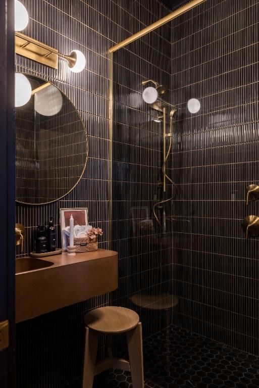 Een schemerige badkamer met ronde lampen, een klein krukje en donkere tegelwanden.