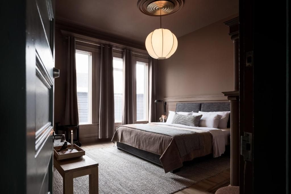 Een schemerige slaapkamer met een bed, gordijnen, een vloerkleed met patroon en hangende papieren lantaarns.