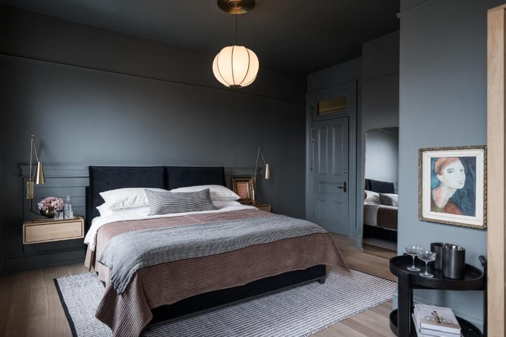 Donkergrijze slaapkamer met een groot bed, nachtkastjes, hanglamp en een vloerkleed met patroon.