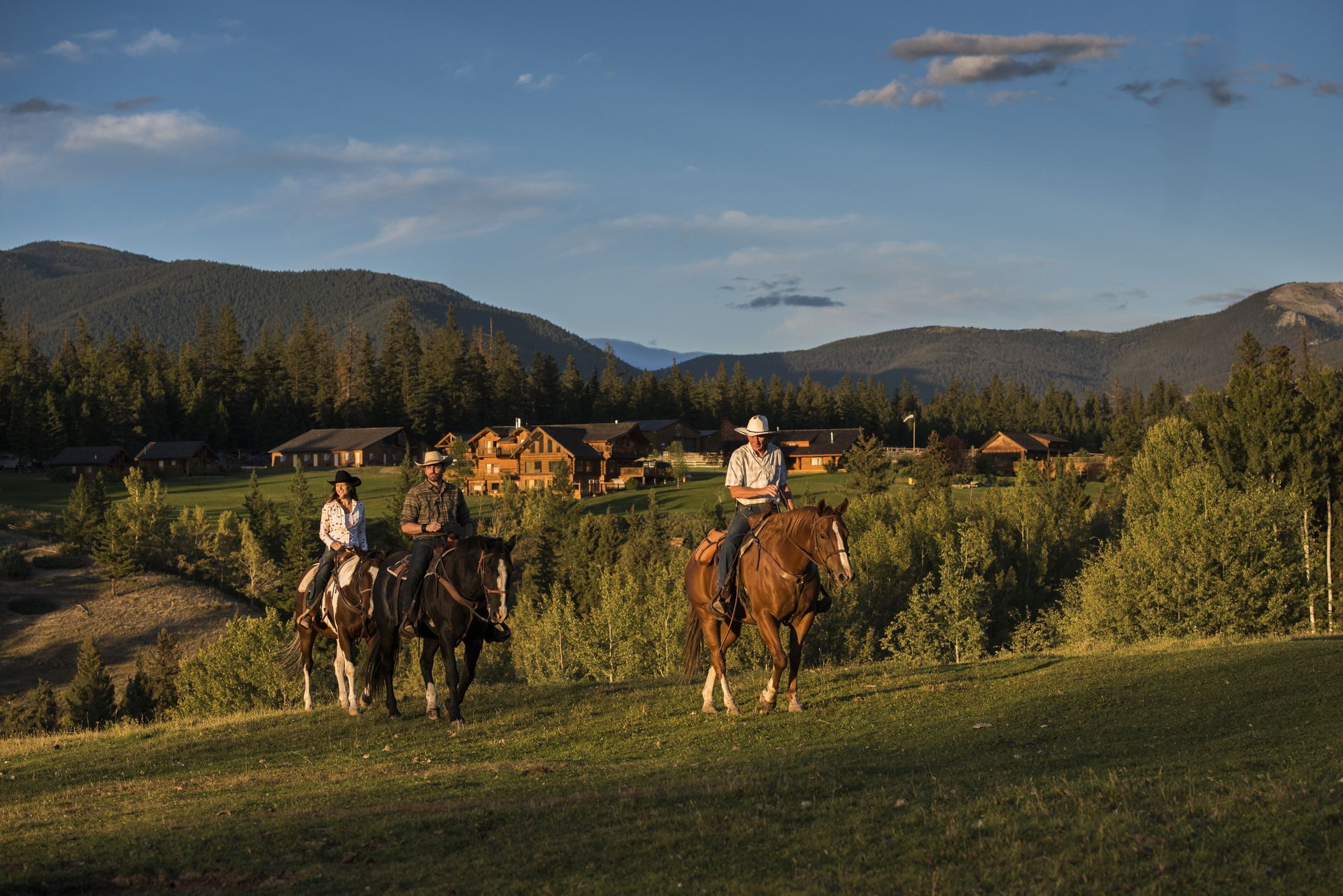 Twee ruiters te paard in een grasveld bij de Echo Valley Ranch met bergen en een dorp op de achtergrond bij zonsondergang.
