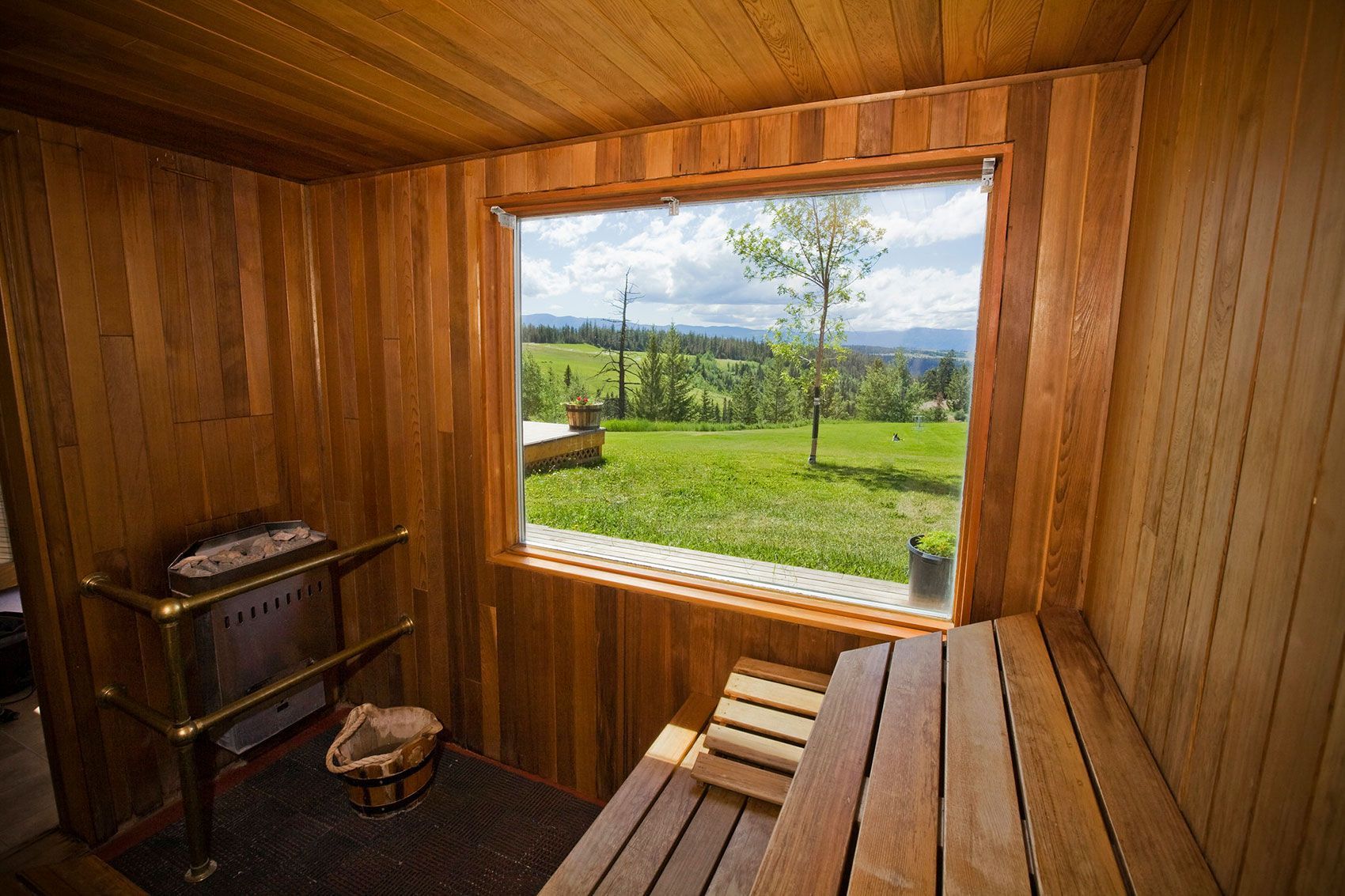 Houten sauna-interieur van Echo Valley Ranch met bank, kachel en groot raam met uitzicht op een groen veld.