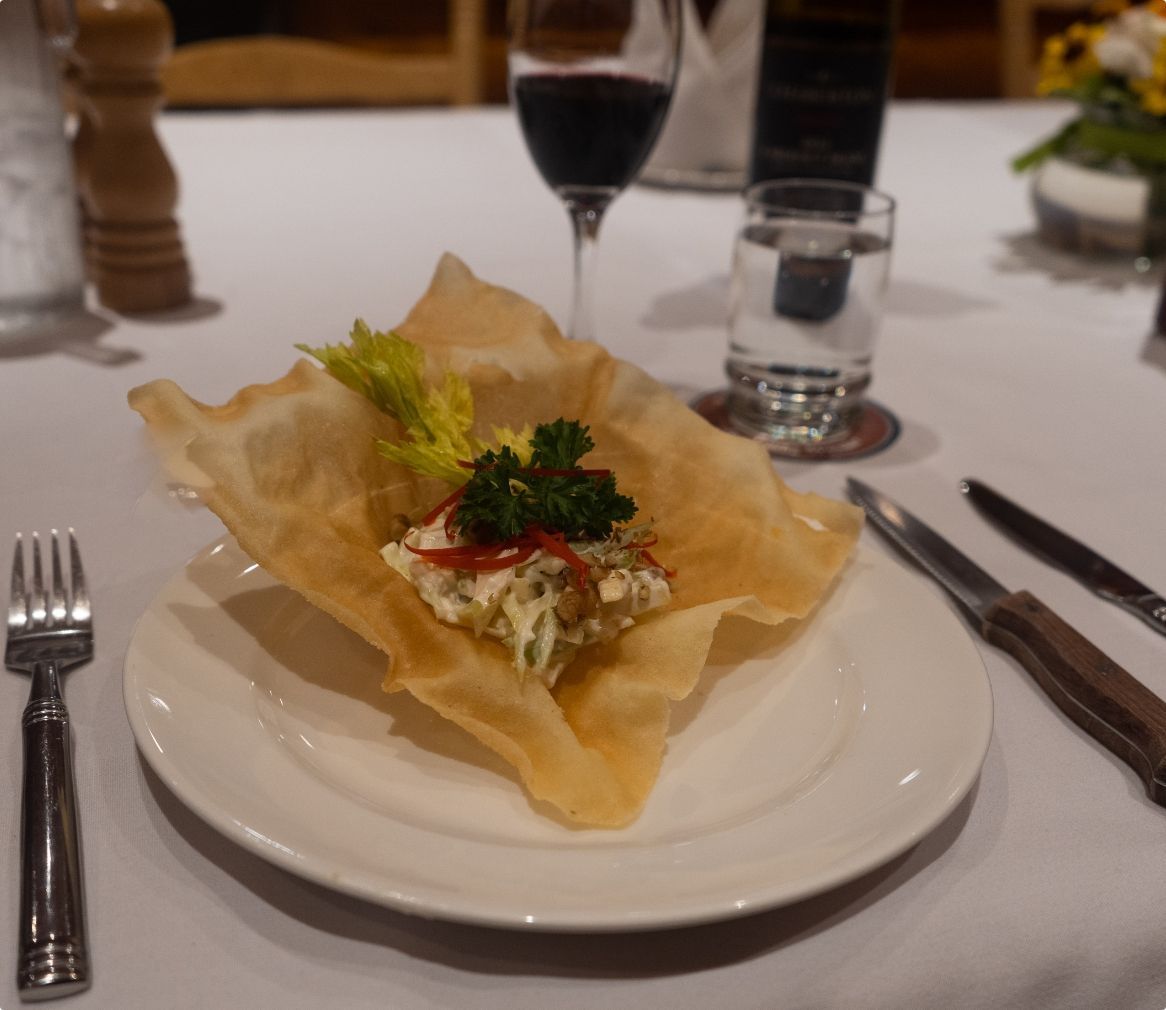 Een gastronomisch voorgerecht bij Echo Valley Ranch in een knapperig bladerdeegbakje op een wit bord, met een wijnglas en bestek op tafel.