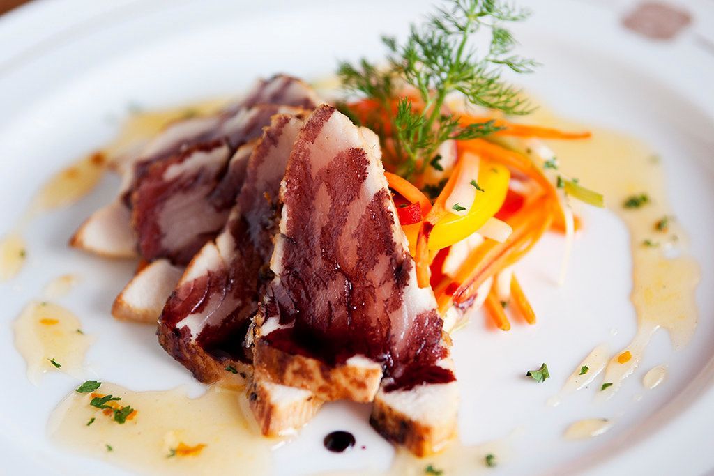 Geroosterde plakjes vlees met kleurrijke groentegarnituur en saus op een wit bord.