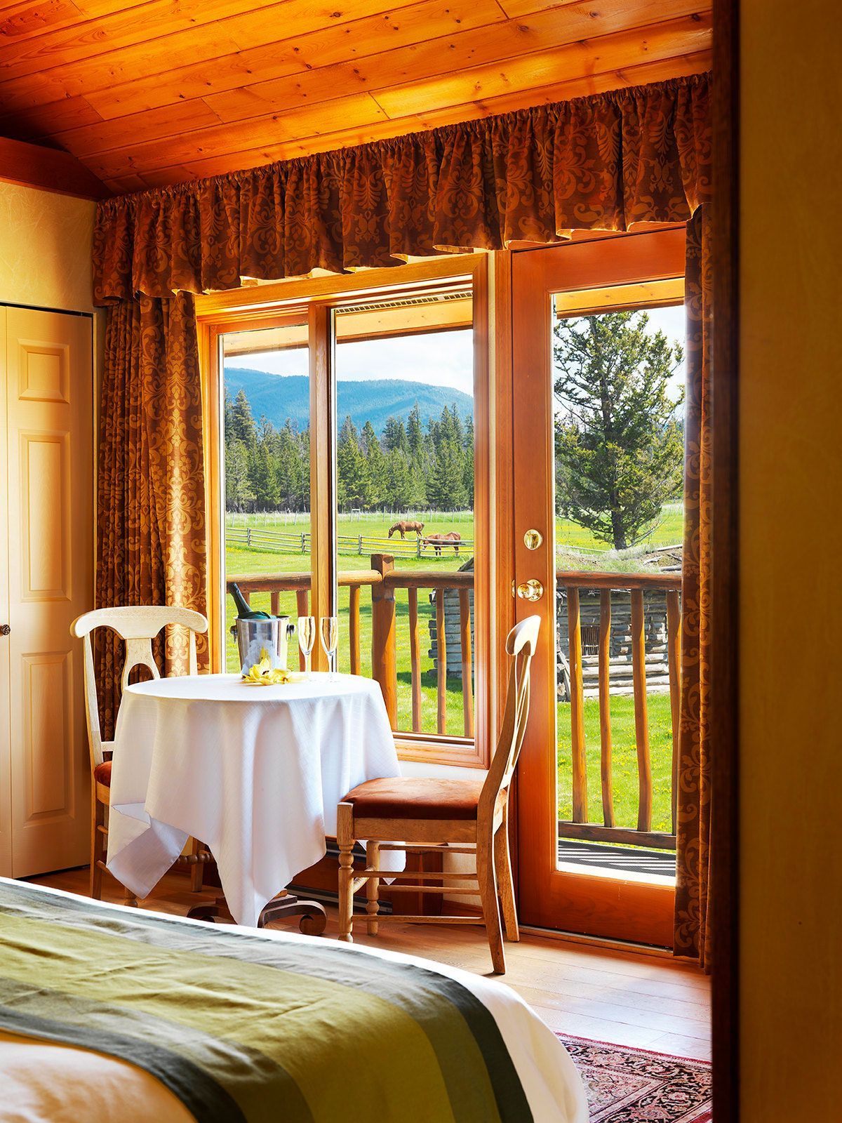 Gezellige slaapkamer van Echo Valley Ranch met een klein tafeltje bij een open deur met uitzicht op een groene weide en de bergen.