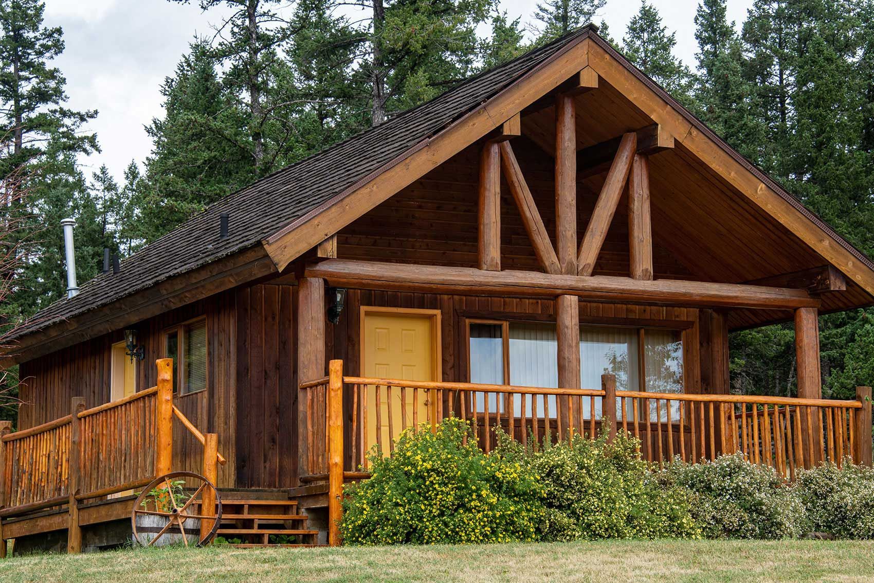 Houten blokhut van Echo Valley Ranch met een overdekte veranda en terras, omgeven door bomen en groen.
