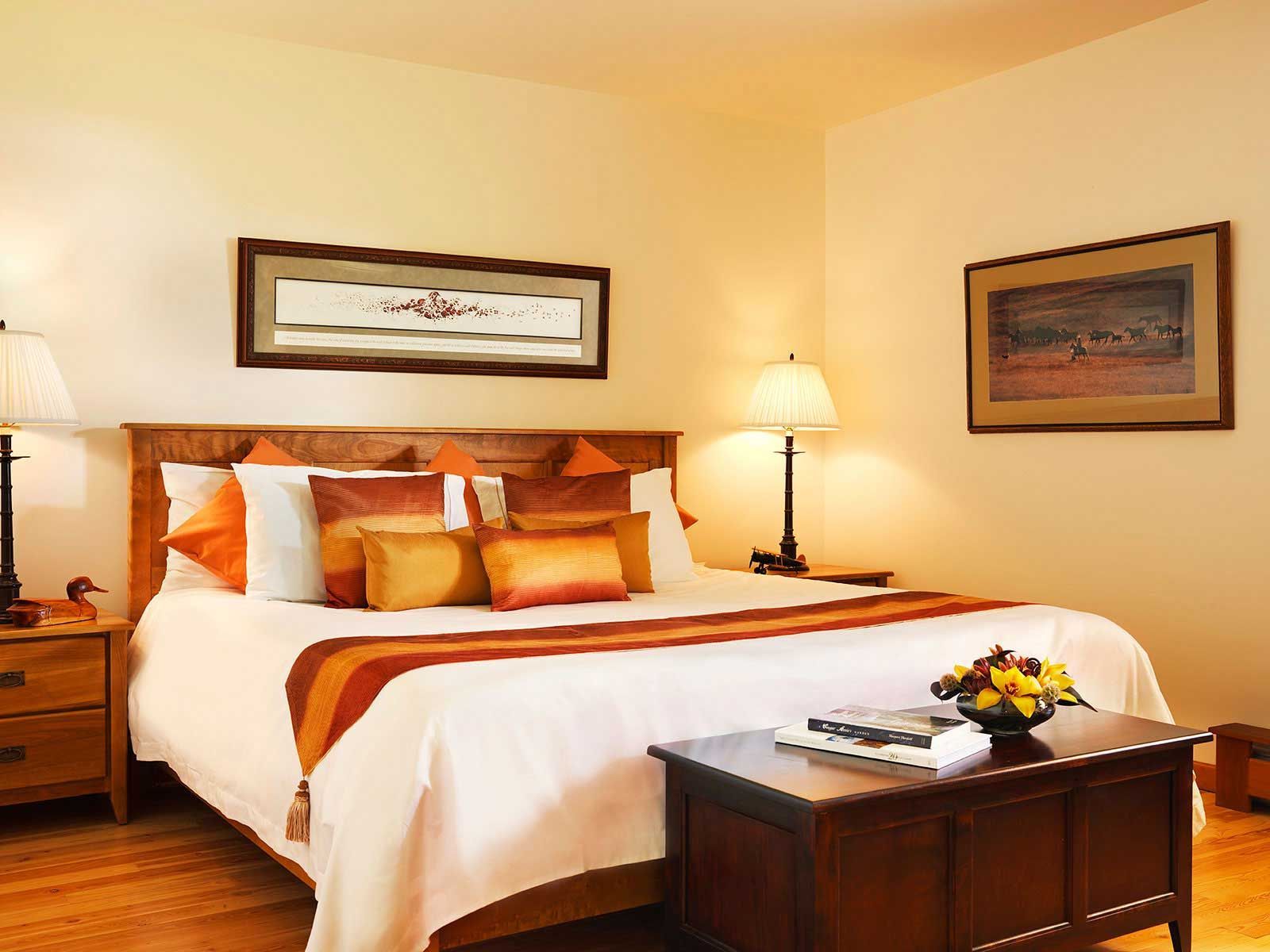 Gezellige slaapkamer van Echo Valley Ranch met een netjes opgemaakt bed, warme verlichting, nachtlampjes en een houten bankje aan het voeteneinde van het bed.