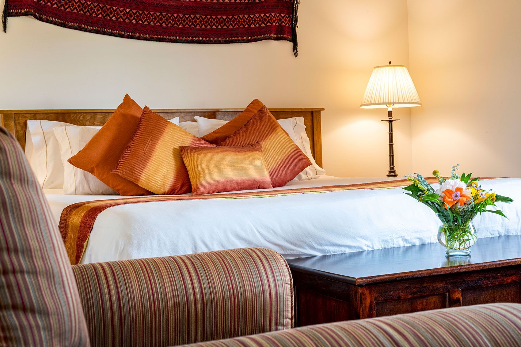 Gezellige slaapkamer van Echo Valley Ranch met een netjes opgemaakt bed, oranje kussens, een nachtlampje en bloemen op een houten tafeltje.
