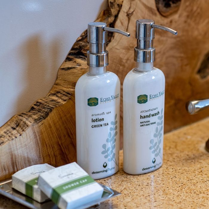 Badkamerartikelen van Echo Valley Ranch op een houten wastafel: lotion, handzeep en zeep op een dienblad.