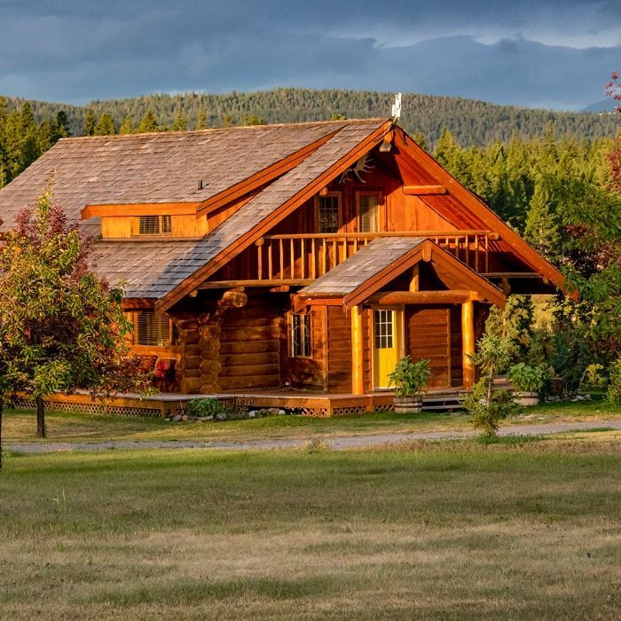 Een bijgebouw van Echo Valley Ranch met een steil dak, gelegen in een grasveld met beboste bergen op de achtergrond.