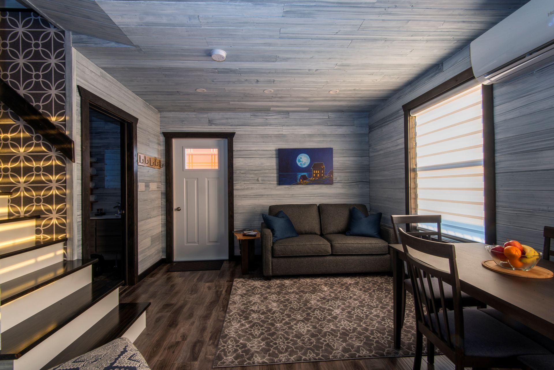 Modern interieur van een blokhut van Escape by the Sea in Newfoundland met een bank, eettafel, wanddecoratie en een witte deur onder een plafond van houten planken.