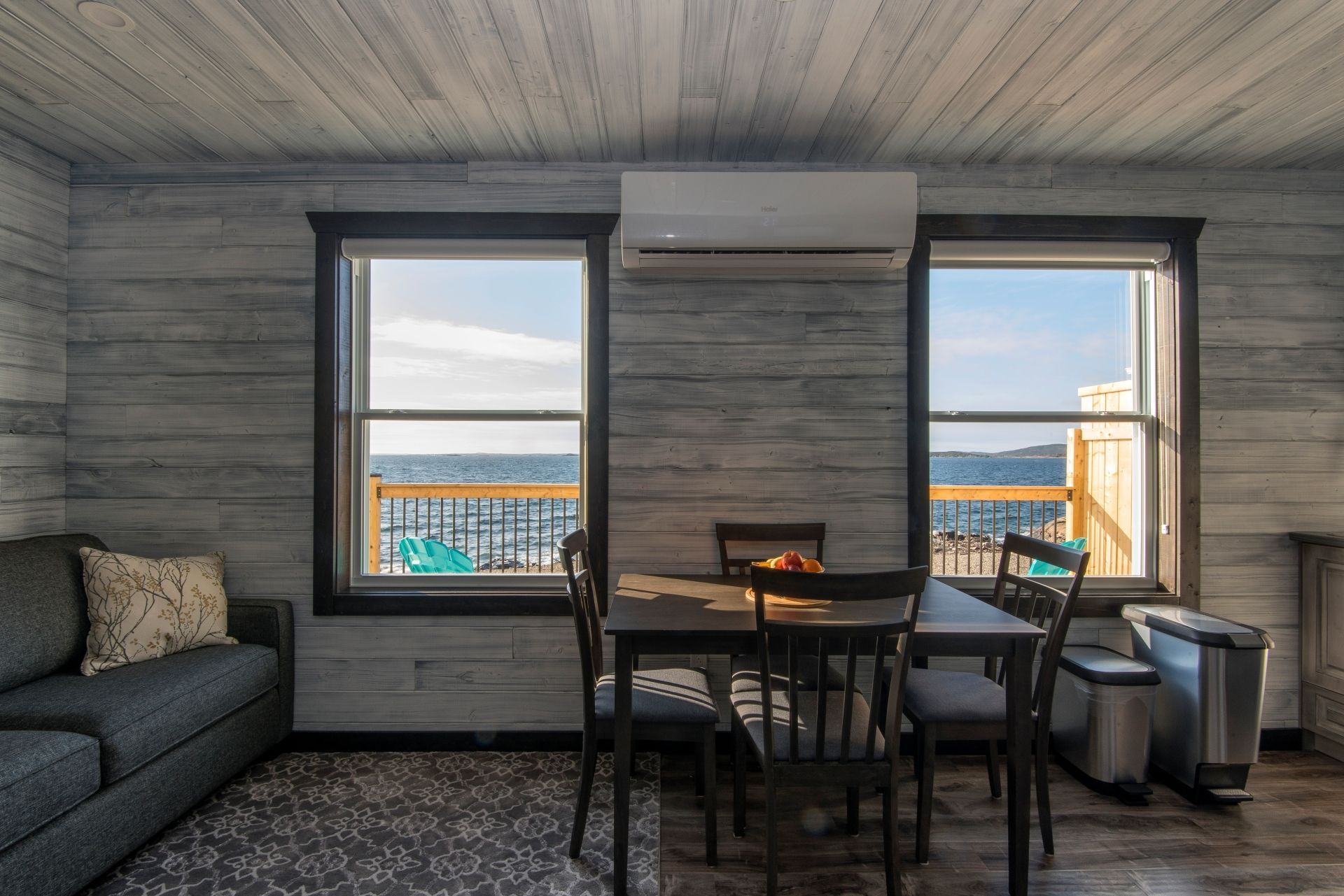 Moderne woonkamer in een huis van Escape by the Sea in Newfoundland met een bank, eettafel, airconditioning en twee ramen met uitzicht op de zee.