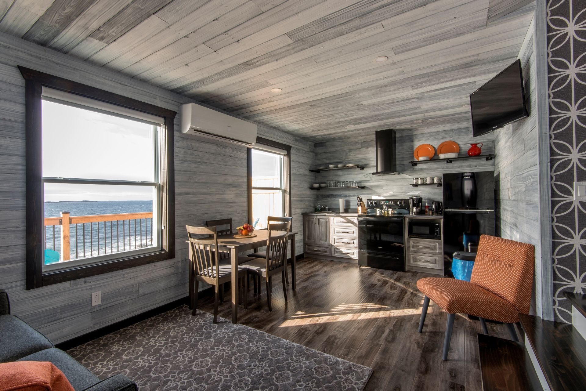 Gezellige grijze keuken in een huis van Escape by the Sea in Newfoundland en eethoek met groot raam dat uitzicht biedt op het water en de bergen.