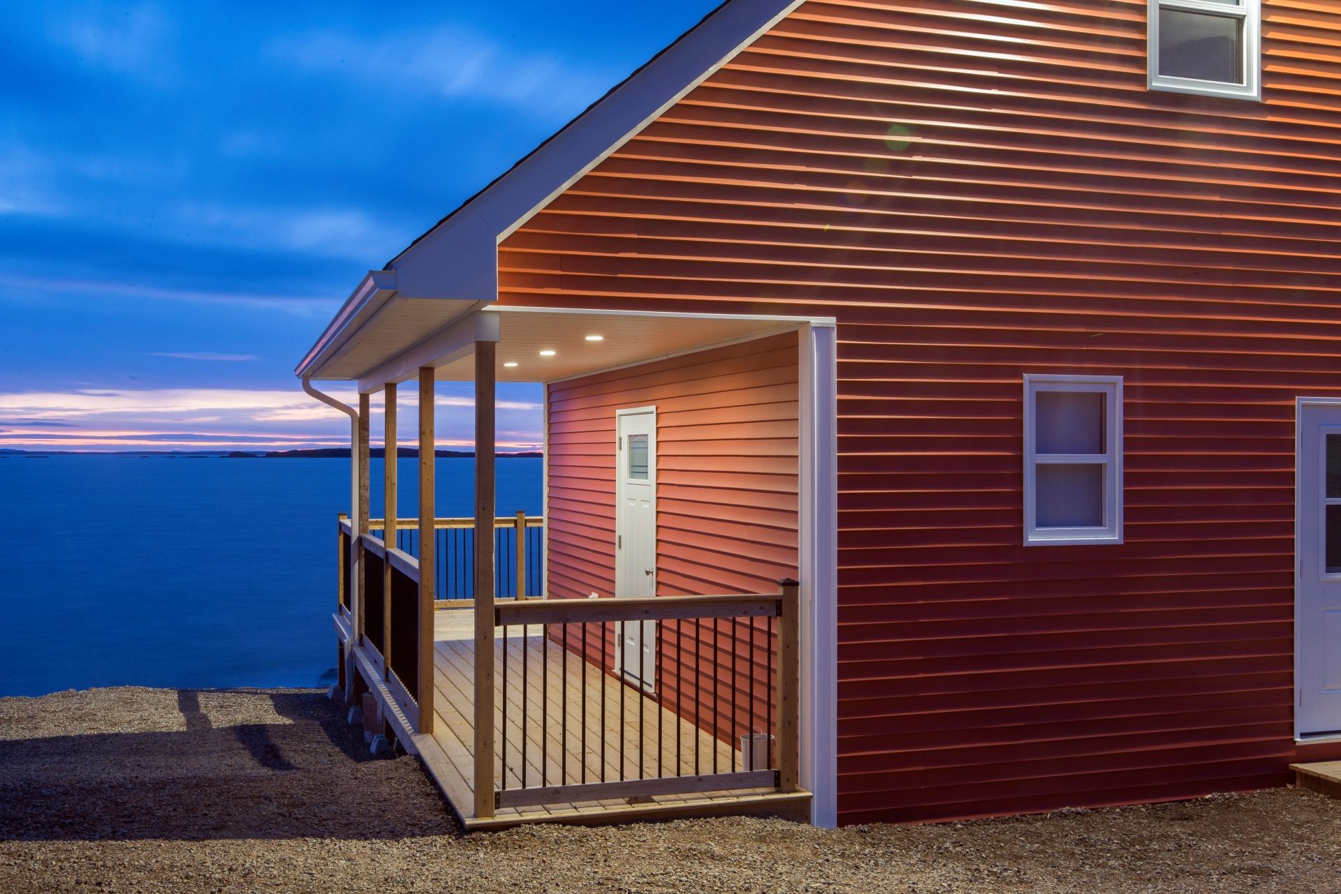 Rood huis aan zee van Escape by the Sea in Newfoundland met veranda die uitzicht biedt op de oceaan bij zonsondergang.
