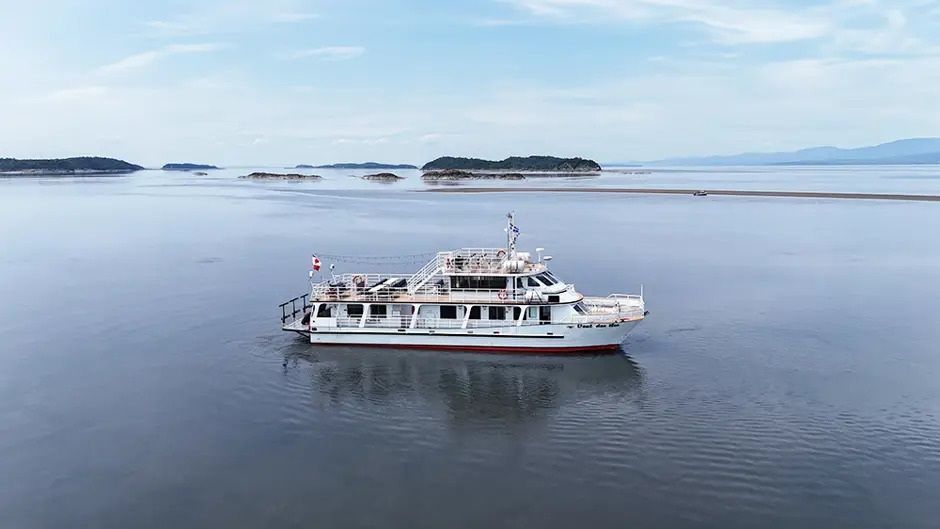 Een witte passagiersboot vaart over kalm blauw water met kleine eilandjes in de verte.