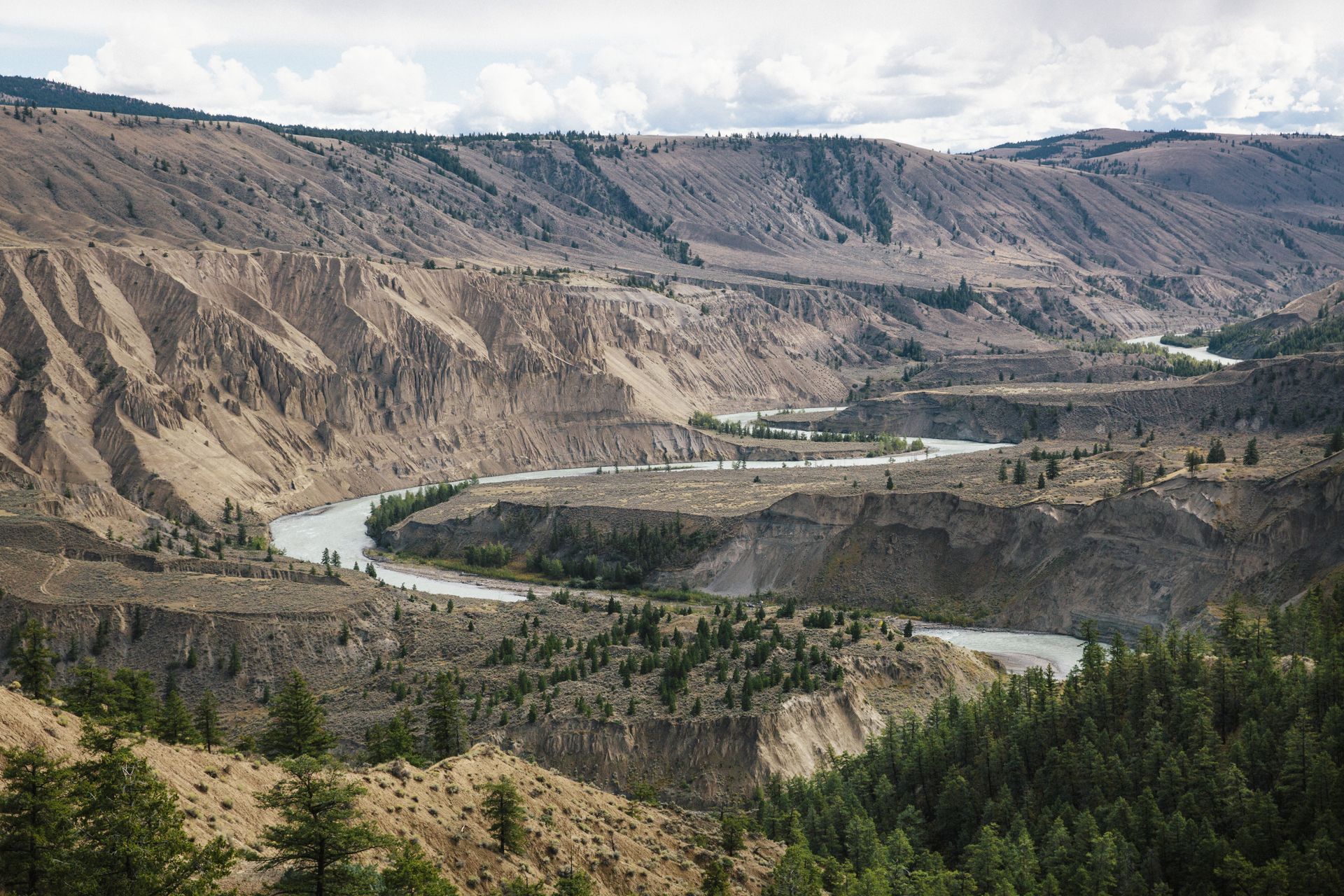 Een kronkelende rivier in de Farwell Canyon nabij Riske Creek stroomt door een ruige kloof met steile bruine heuvels en stukjes groen bos.