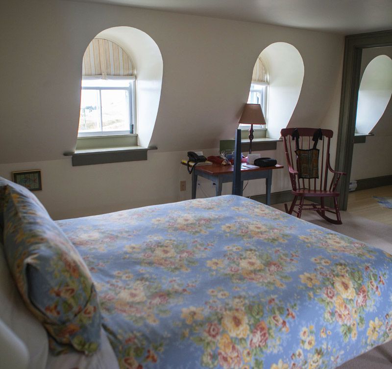 Slaapkamer van Fisher's Loft Inn in Port Rexton met een bed, een sprei met bloemenprint, twee boogvensters en een klein bureau met een lamp.