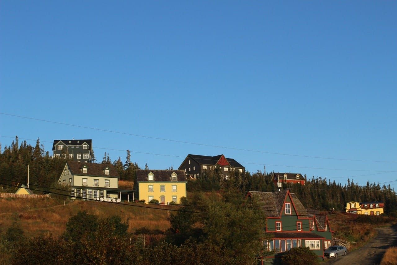Huizen van Fisher's Loft Inn in Port Rexton op een heuvel onder een helderblauwe hemel, met bomen en een voorgrond in herfstkleuren.