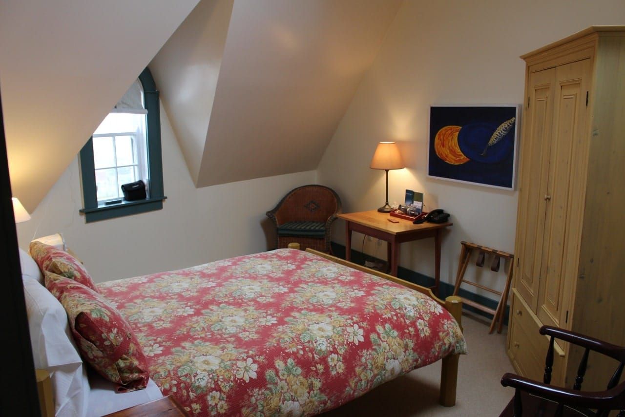 Gezellige slaapkamer van Fisher's Loft Inn in Port Rexton met een bloemensprei, schuin plafond, klein raam en houten dressoir met lamp.
