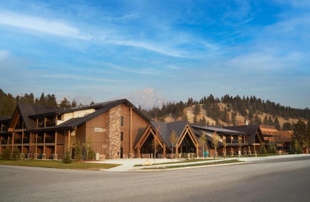 Rustieke lodgegebouwen met houten balken en lichtbruine muren onder een blauwe hemel, naast een geplaveide weg en dennenbomen van Forest Park Hotel, Jasper